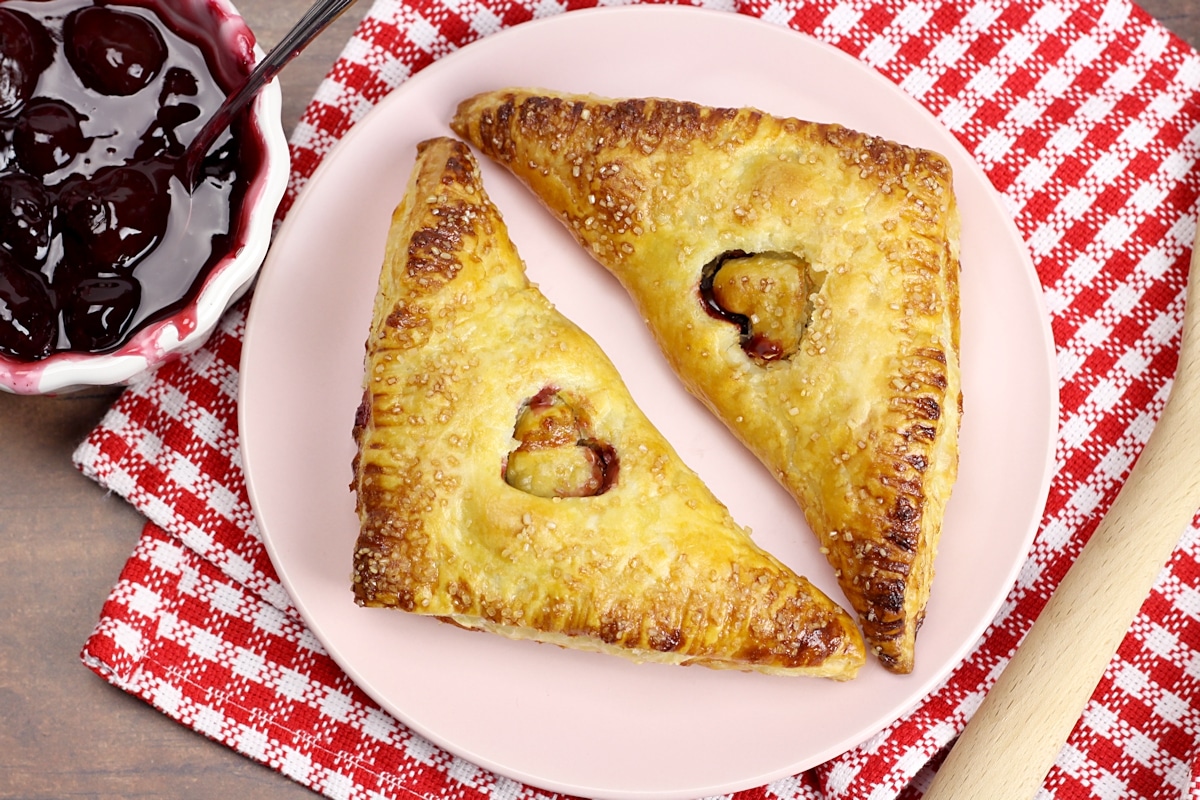 Two turnovers on a pink plate with a red checkered towel.