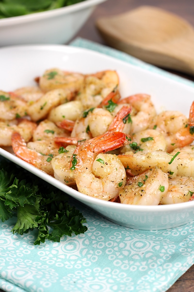 Shrimp coated in garlic butter and parsley, on a white serving plate.