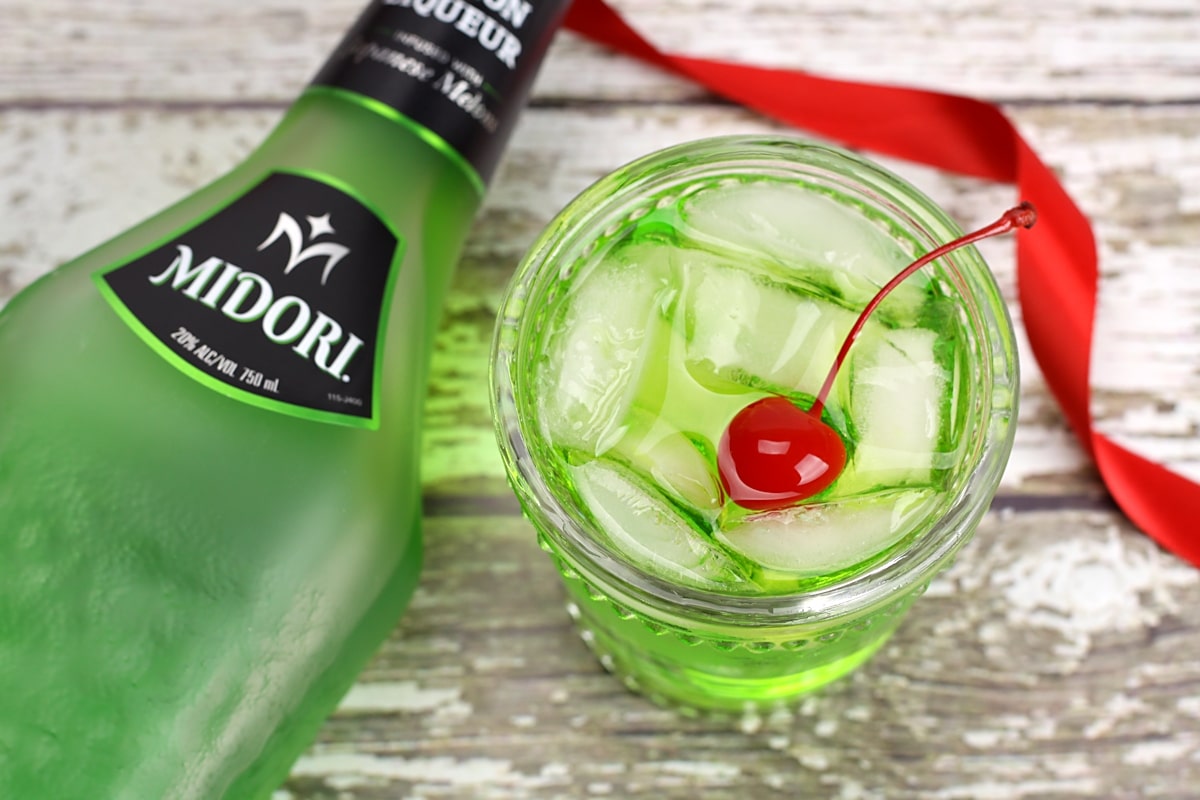 A bottle of midori liqueur beside a green cocktail.