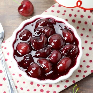 White bowl of cherry pie filling on a wooden counter top.