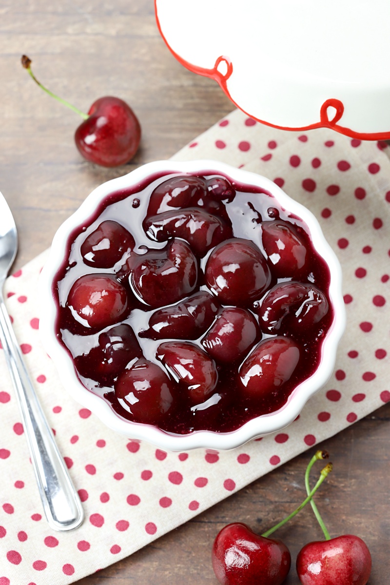 White bowl of cherry pie filling on a wooden counter top.