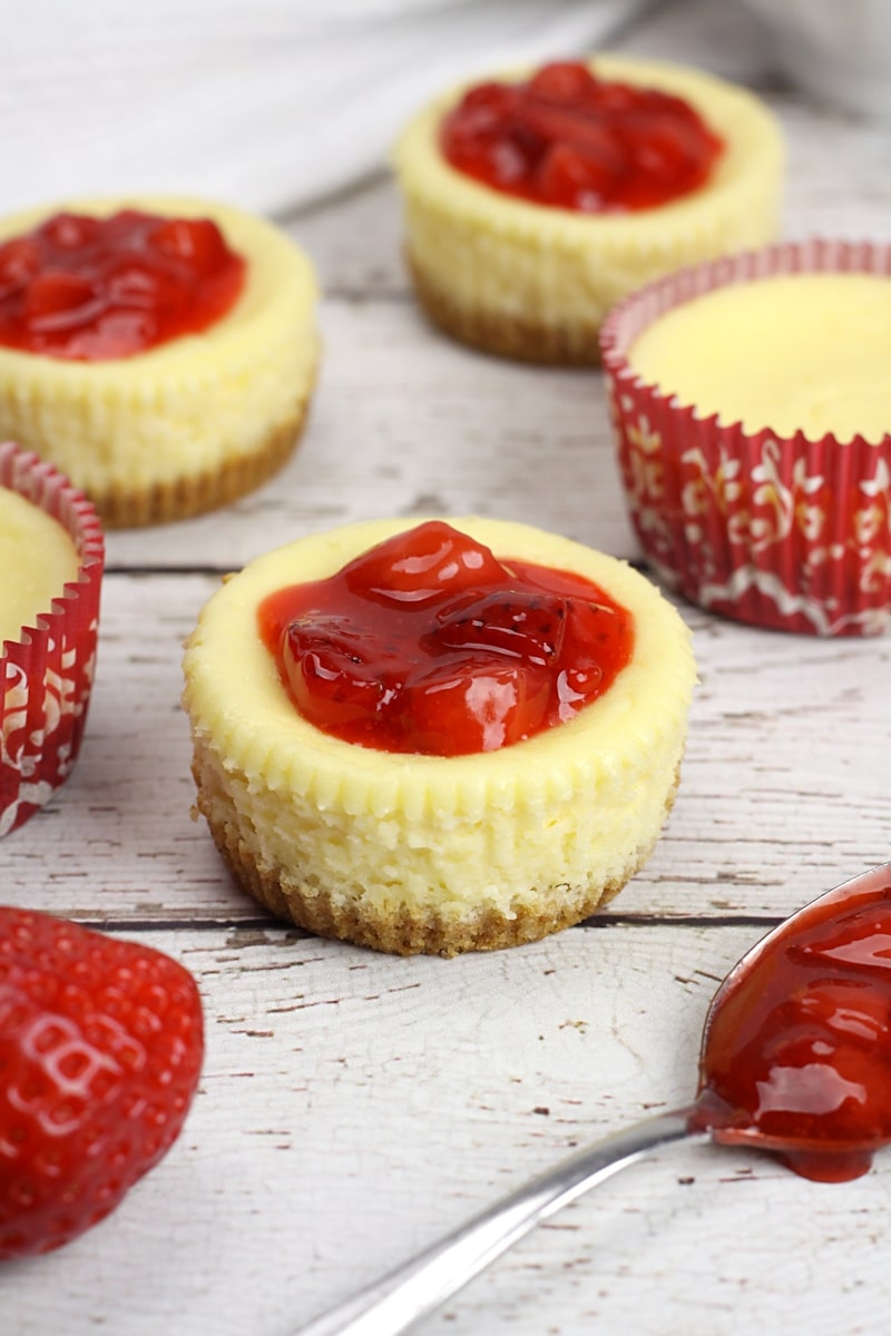 Single serve cheesecakes topped with strawberries on a wood counter top.