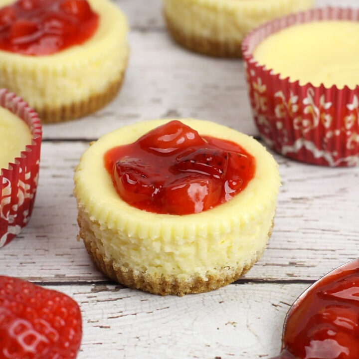 Mini cheesecakes topped with strawberries on a wood counter top.
