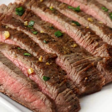 Sliced flank steak topped with garlic butter and fresh parsley.