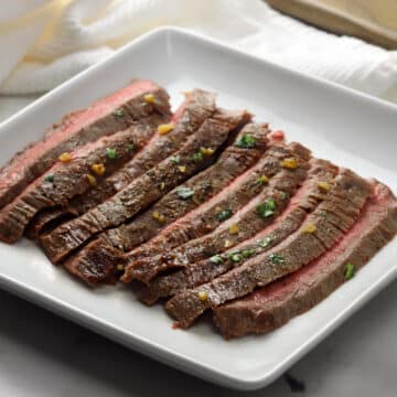 Pan seared flank steak sliced on a white serving plate.