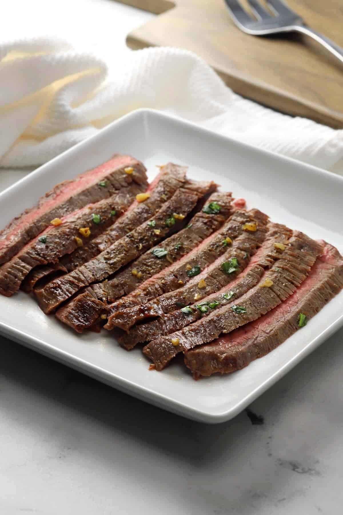 Pan seared flank steak sliced on a white serving plate.