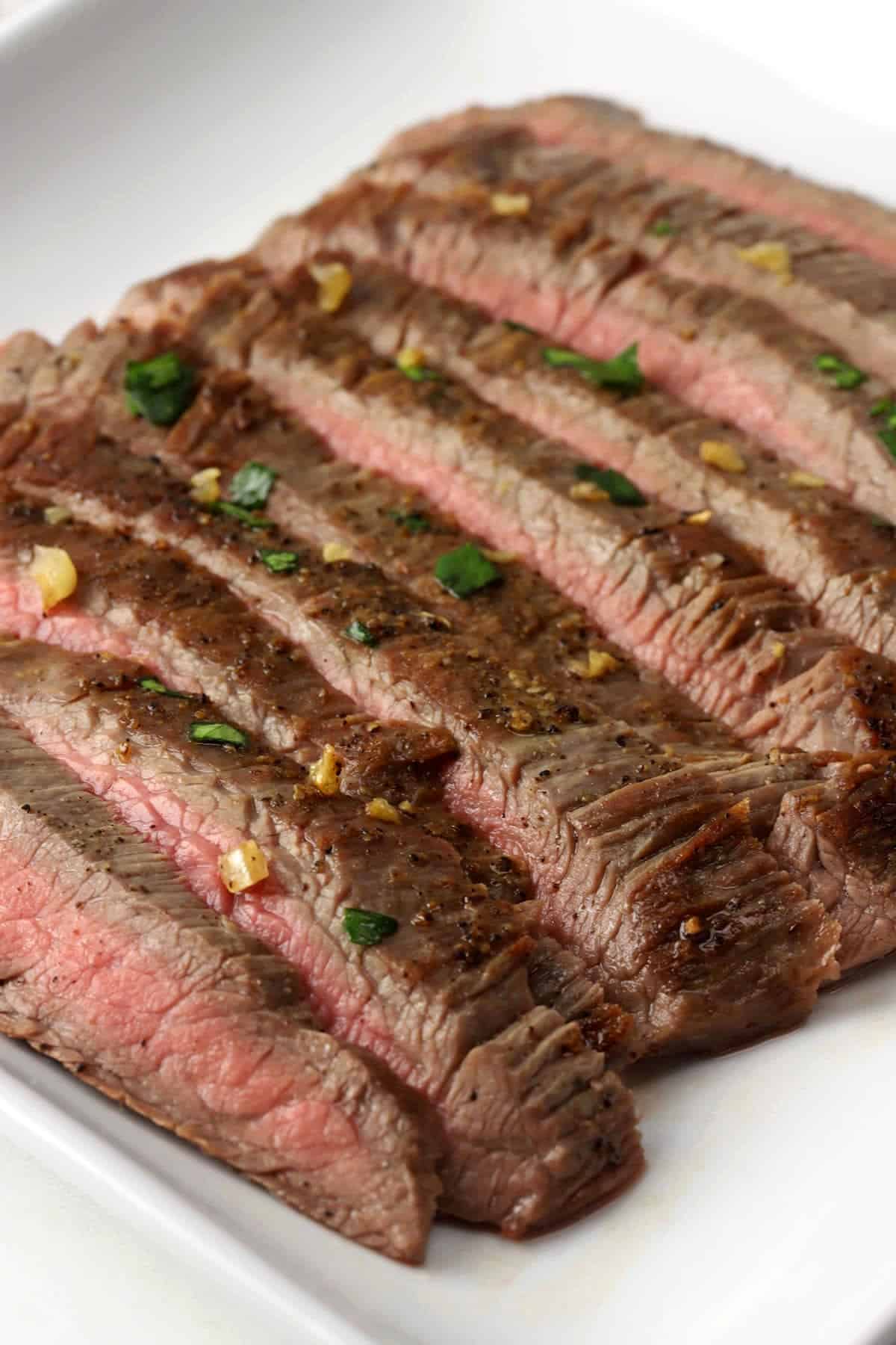 Sliced flank steak topped with garlic butter and fresh parsley.