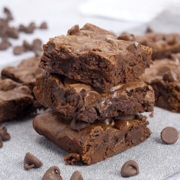 A stack of three brownies on a towel, with chocolate chips.