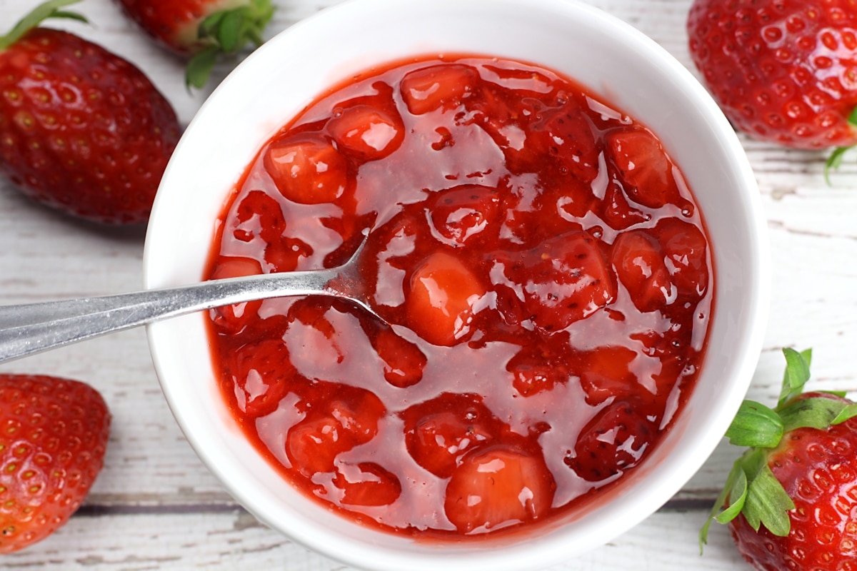 A white bowl filled with strawberries and a spoon.