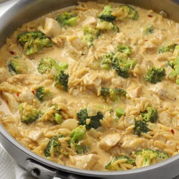 A metal saute pan filled with cheesy orzo with broccoli and chicken.