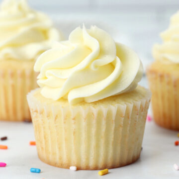 Close up of a vanilla cupcake with rainbow sprinkles on the counter.