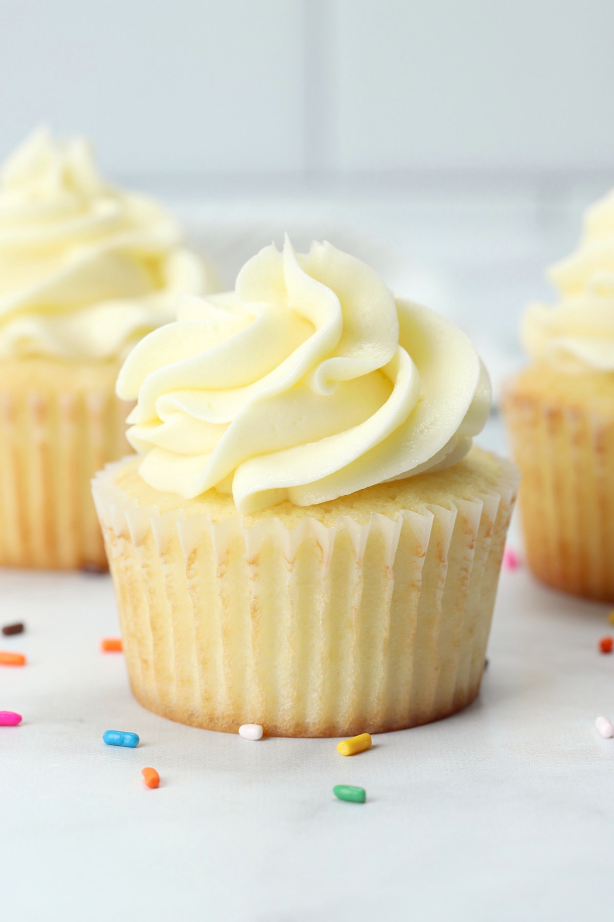 Close up of a vanilla cupcake with rainbow sprinkles on the counter.