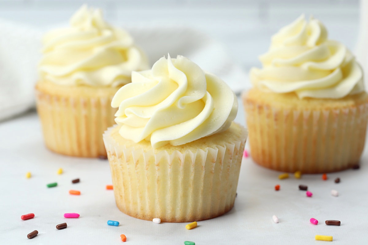 Vanilla cupcakes on a marble counter top with rainbow sprinkles.