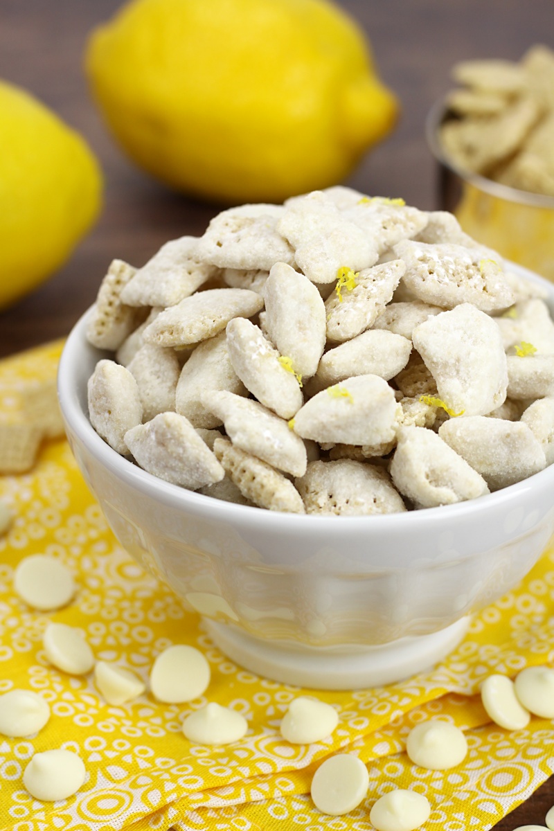 Bowl of puppy chow surrounded by white chocolate chips and lemons.