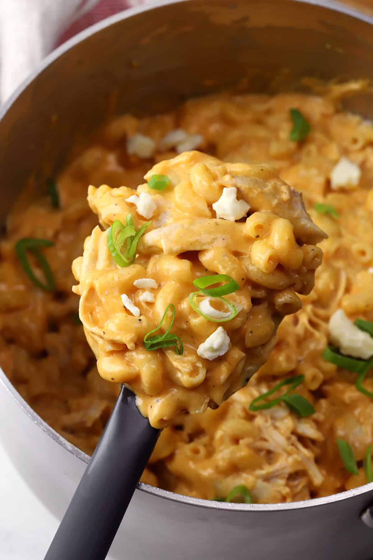 A spoon filled with buffalo chicken mac and cheese over a pot filled with more mac and cheese.