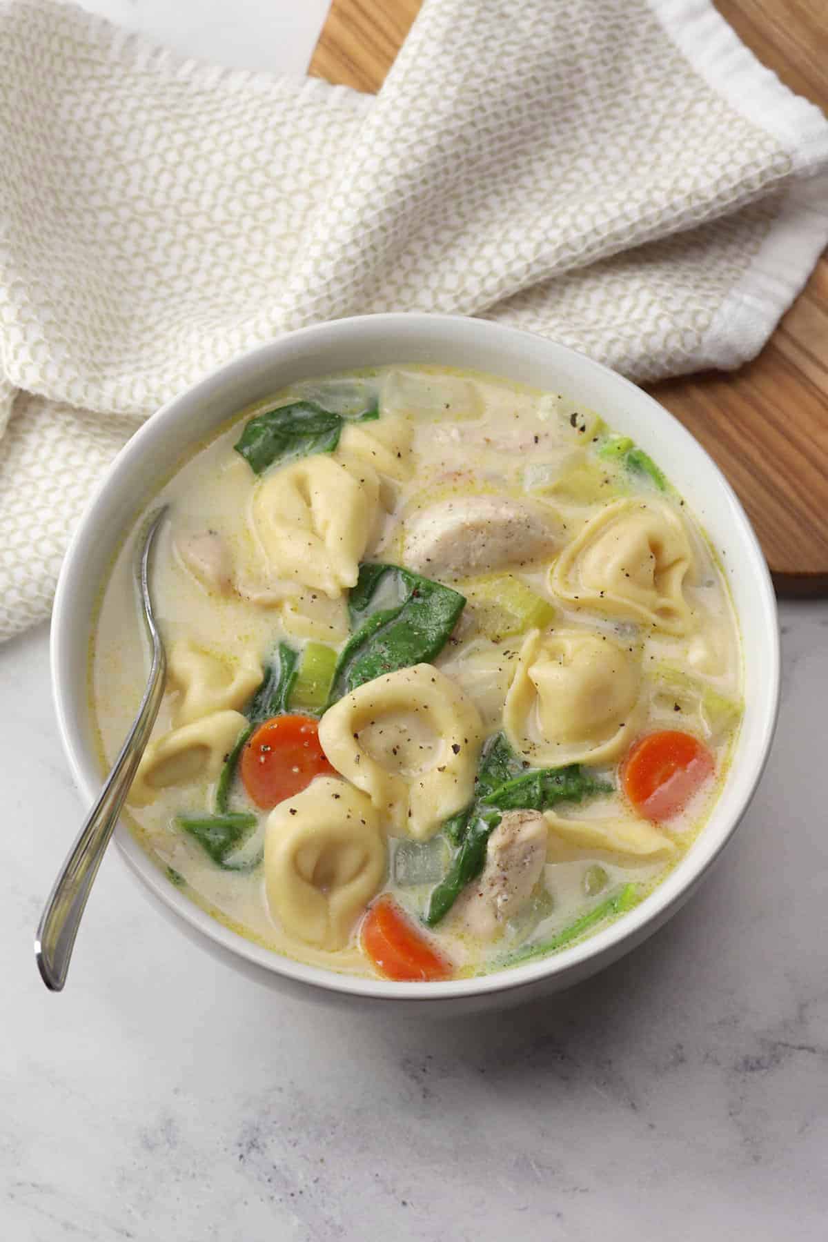 A white bowl filled with creamy chicken tortellini soup and a metal spoon.