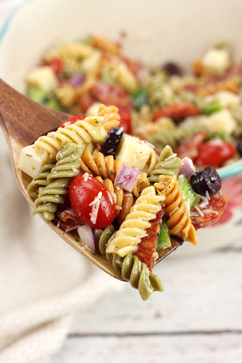A spoonful of classic pasta salad with rotini, cherry tomatoes, olives, pepperoni, and mozzarella cheese.