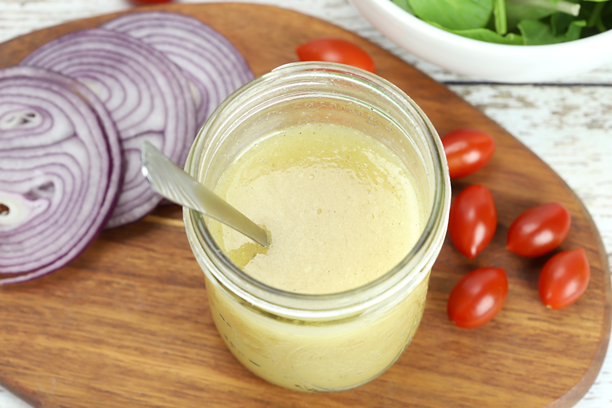 A jar of apple cider vinaigrette on a cutting board with fresh vegetables.