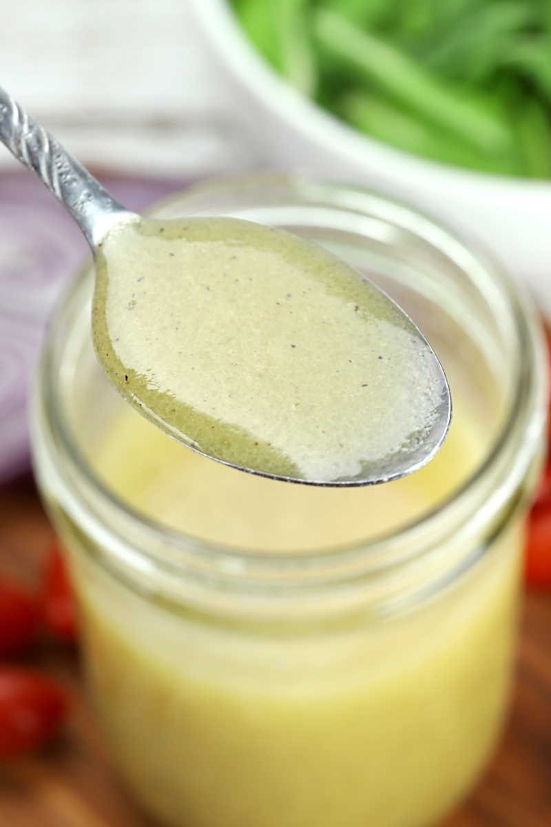 A metal spoon filled with apple cider vinaigrette dressing.