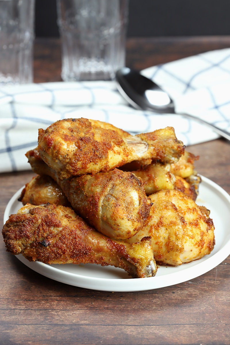 A pile of drumsticks on a white plate, on a wooden kitchen countertop