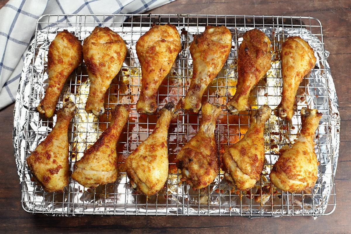 Sheet pan topped with a cooling rack topped with a dozen chicken drumsticks.