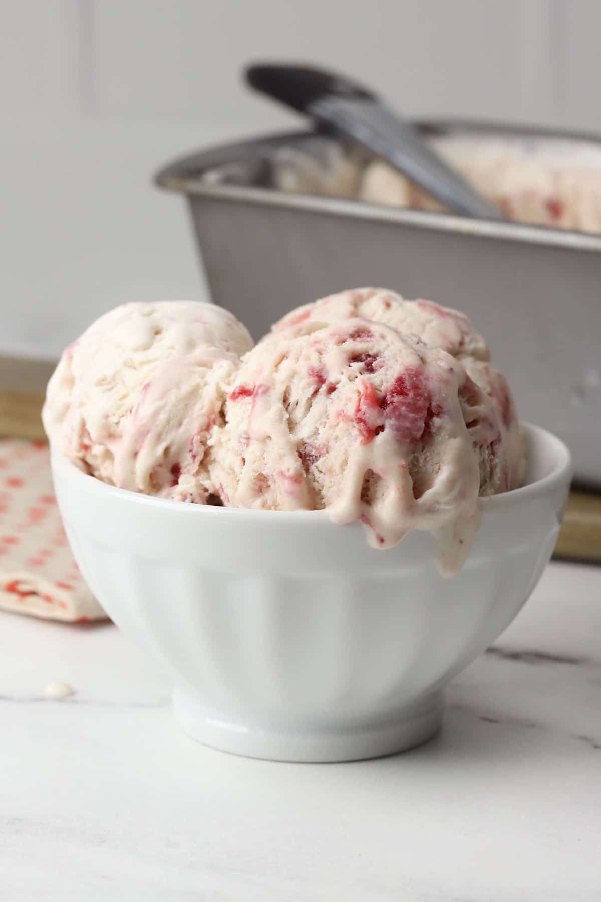 White bowl filled with scoops of strawberry ice cream.