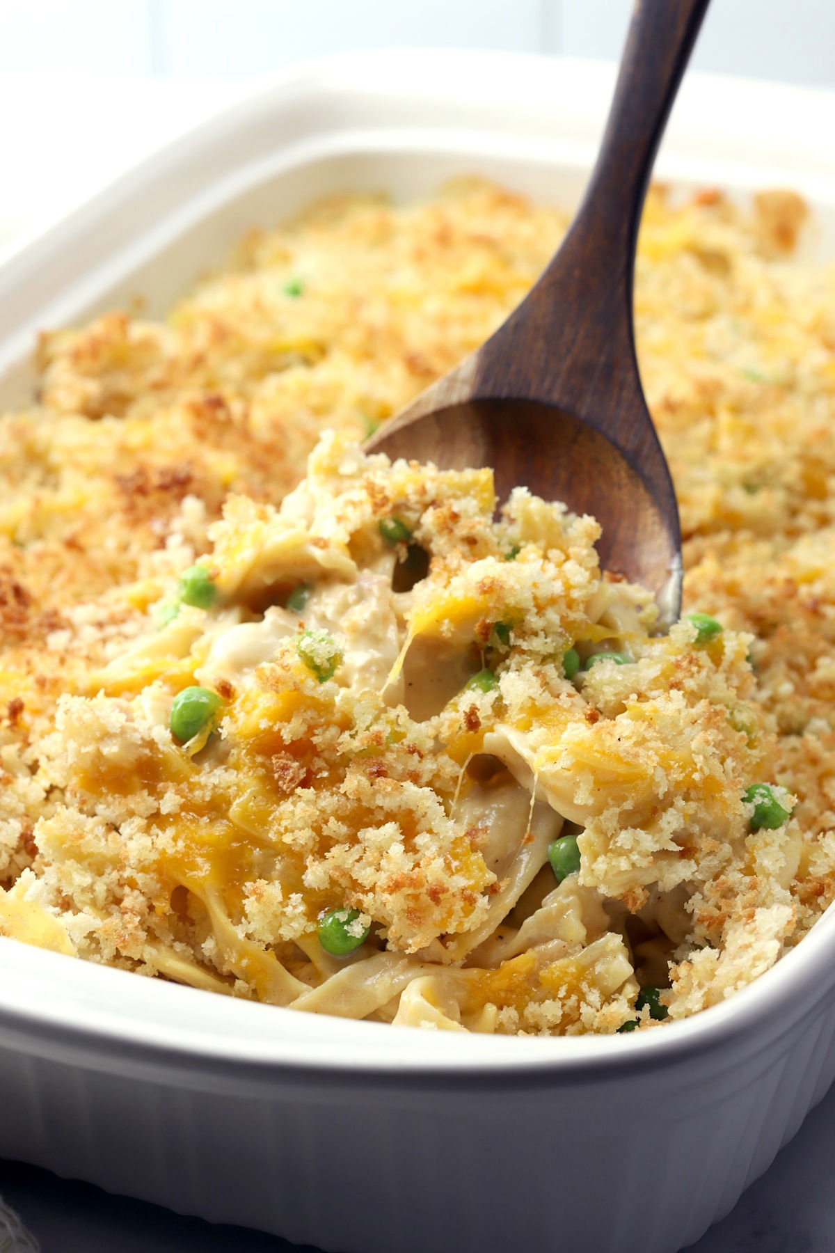 Wooden spoon scooping a serving of a noodle casserole.