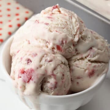 Scoops of strawberry ice cream melting in a bowl.
