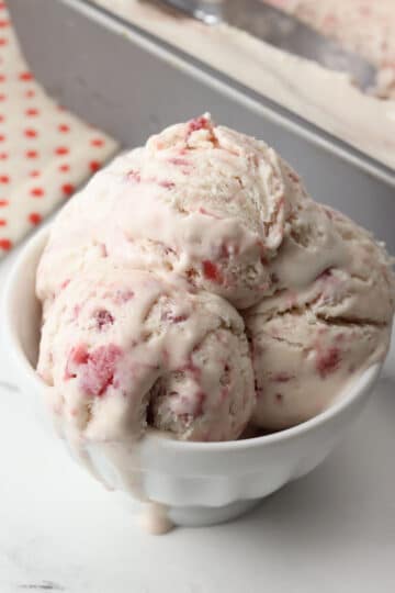 Scoops of strawberry ice cream melting in a bowl.