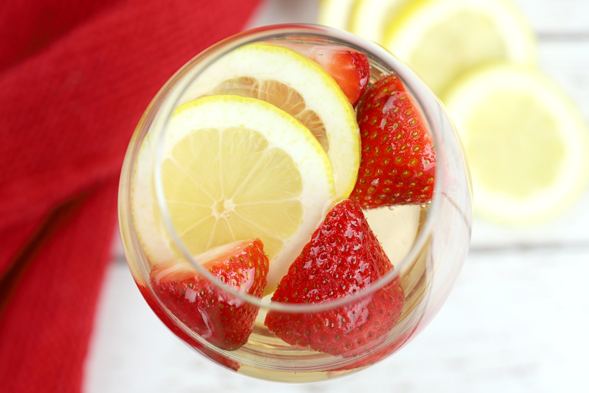 Strawberry slices and lemon slices floating in a wine glass