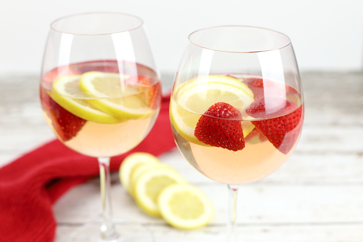 Two glasses of strawberry lemon rose sangria with lemon slices in the background.