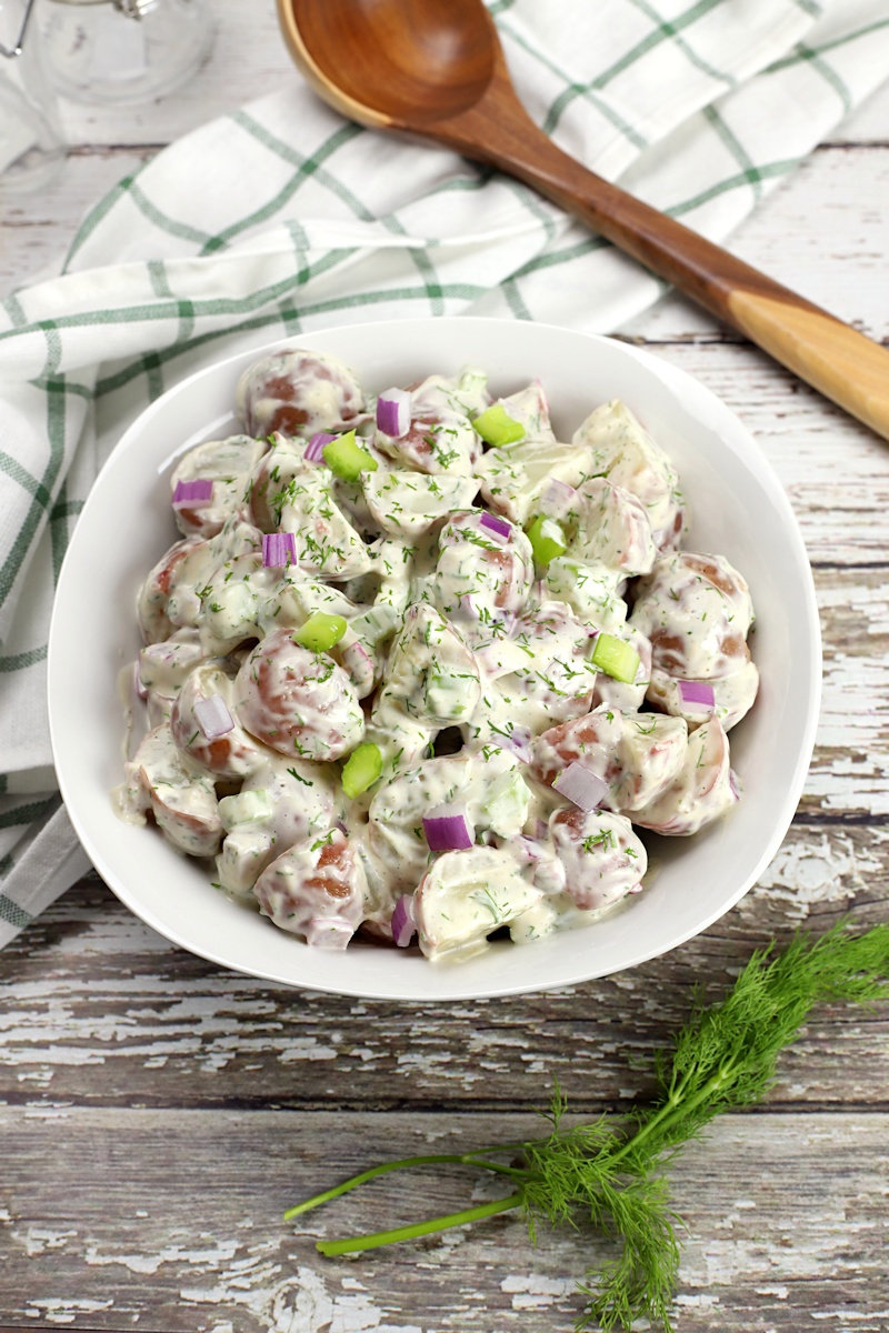 Bowl filled with dill potato salad on a white wood counter top.