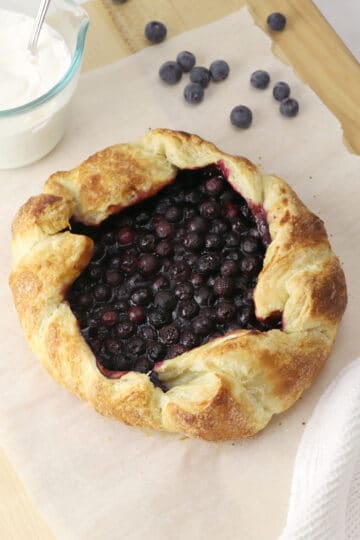 A whole blueberry galette on a wooden cutting board.