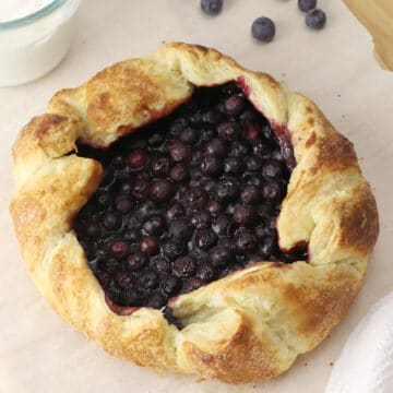 A whole blueberry galette on a wooden cutting board.