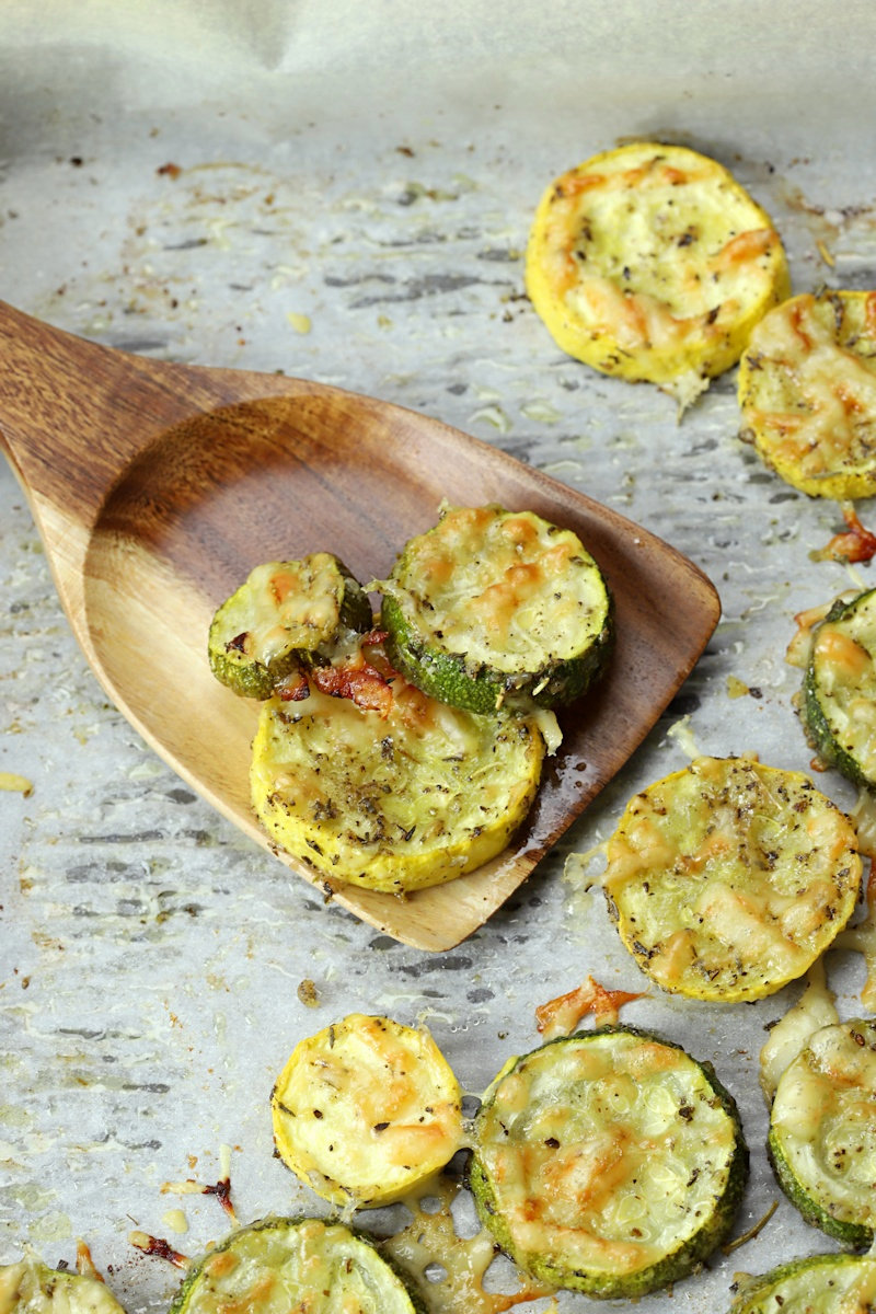 Wooden spatula scooping zucchini and yellow squash from sheet pan.