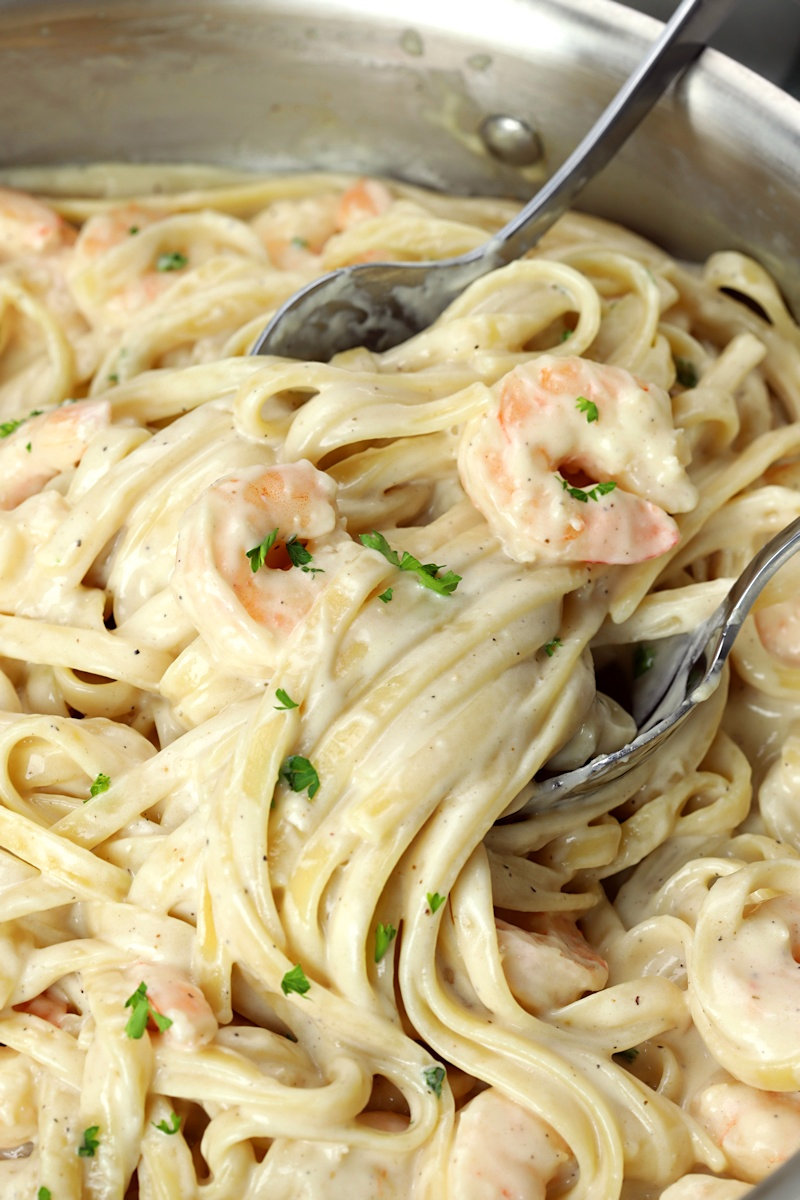 Serving spoon and fork scooping up a serving of pasta and shrimp.