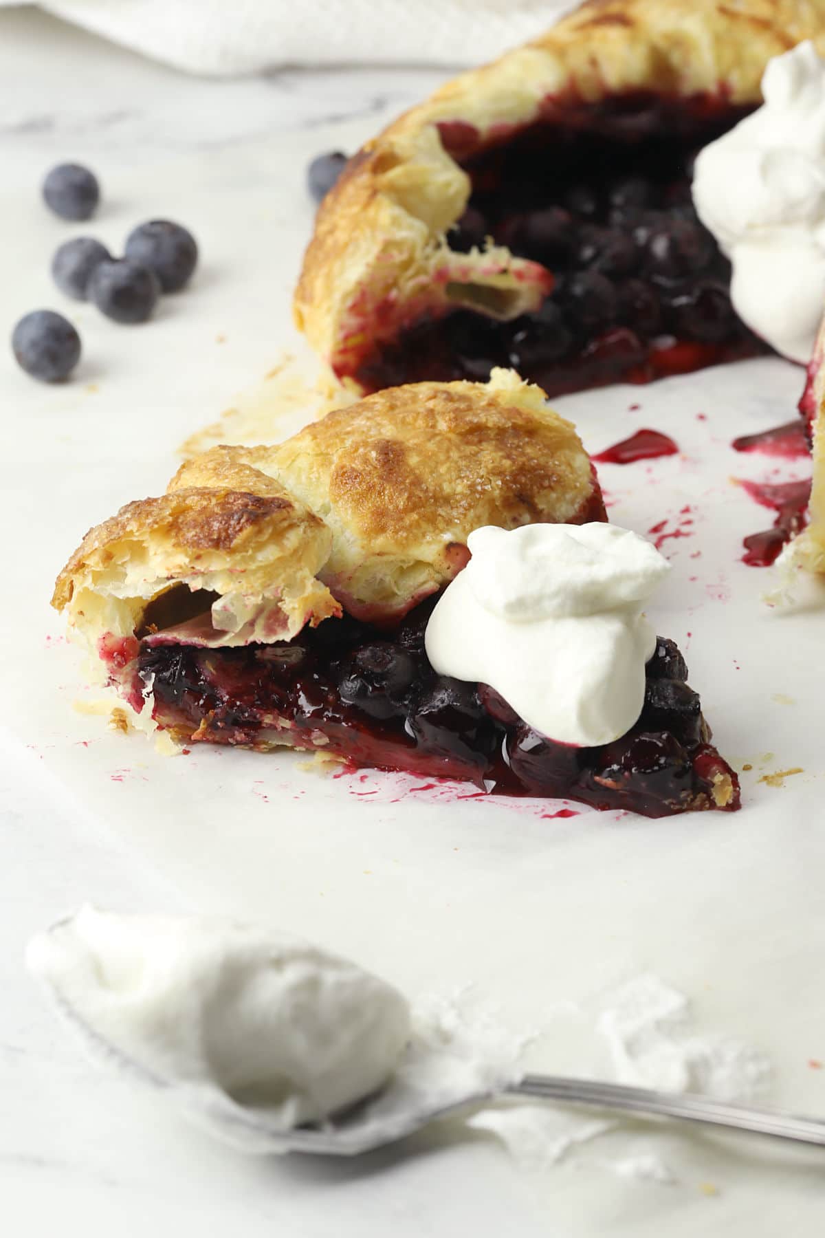 A slice of puff pastry blueberry galette topped with whipped cream.