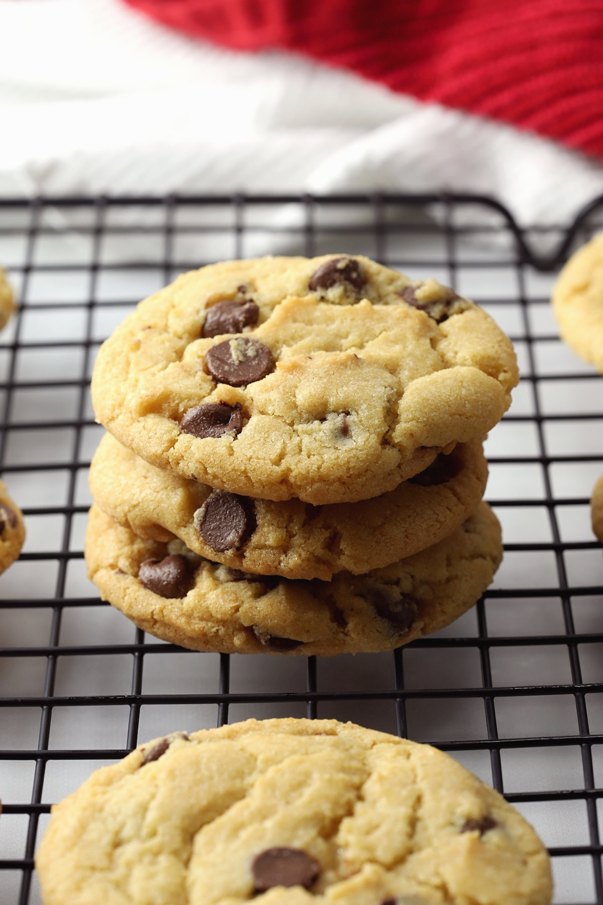 A stack of three chocolate chip cookies on a cooling rack.