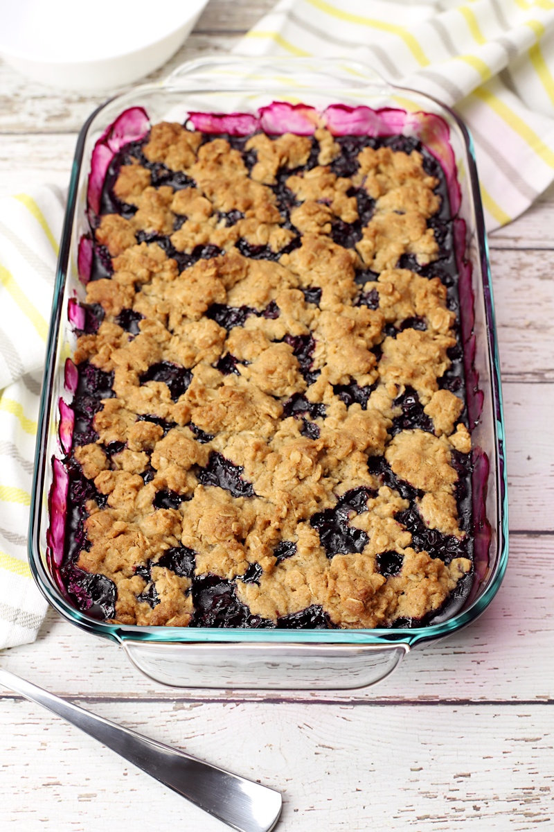 A baked pan of blueberry crisp on a white wood counter top.