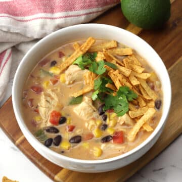 A bowl of creamy chicken tortilla soup on a wooden cutting board.