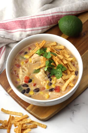 A bowl of creamy chicken tortilla soup on a wooden cutting board.