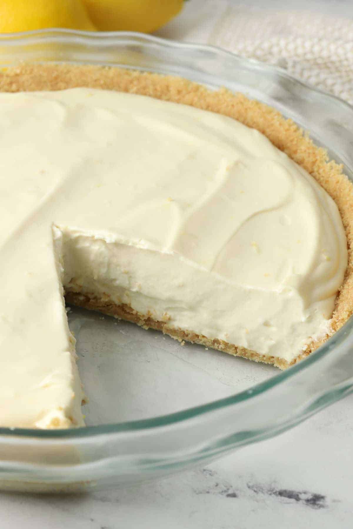 Lemon icebox pie in a glass pie dish with one slice missing.
