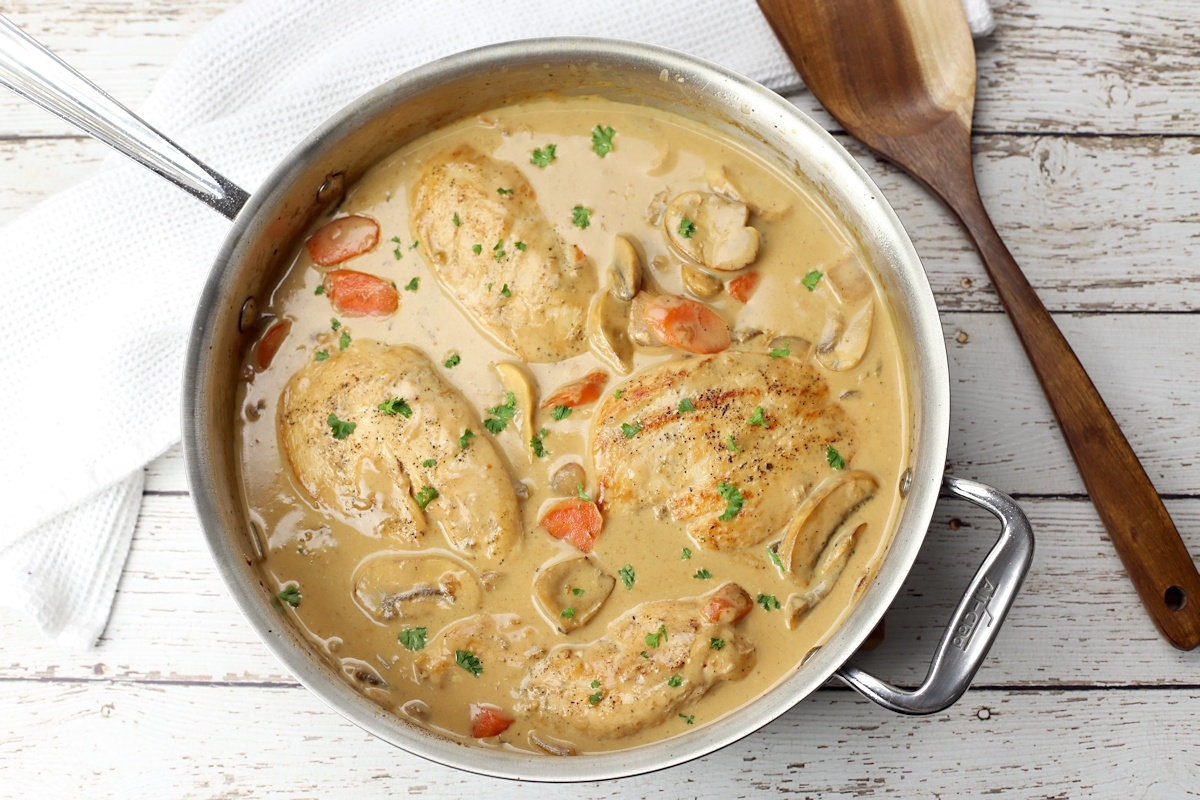 Chicken breasts, carrots, and mushrooms in a creamy white sauce in a saute pan.