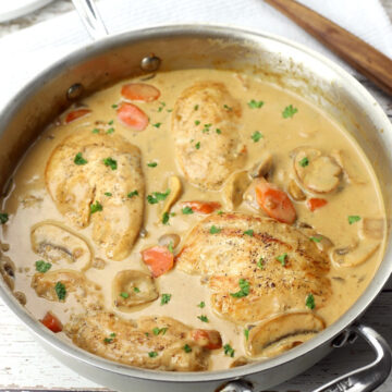 Finished chicken fricassee in a saute pan on a white wood counter top.