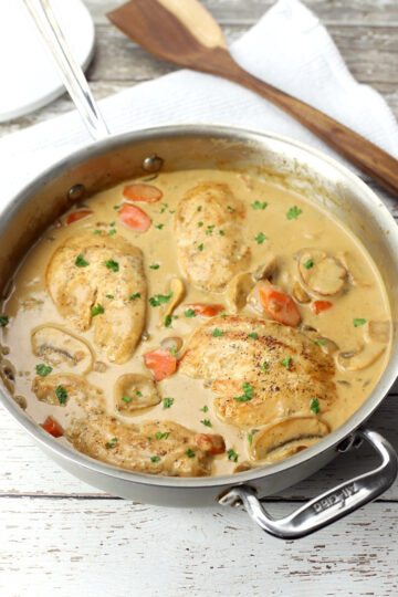 Finished chicken fricassee in a saute pan on a white wood counter top.