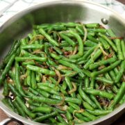 A saute pan of green beans on a wooden counter.