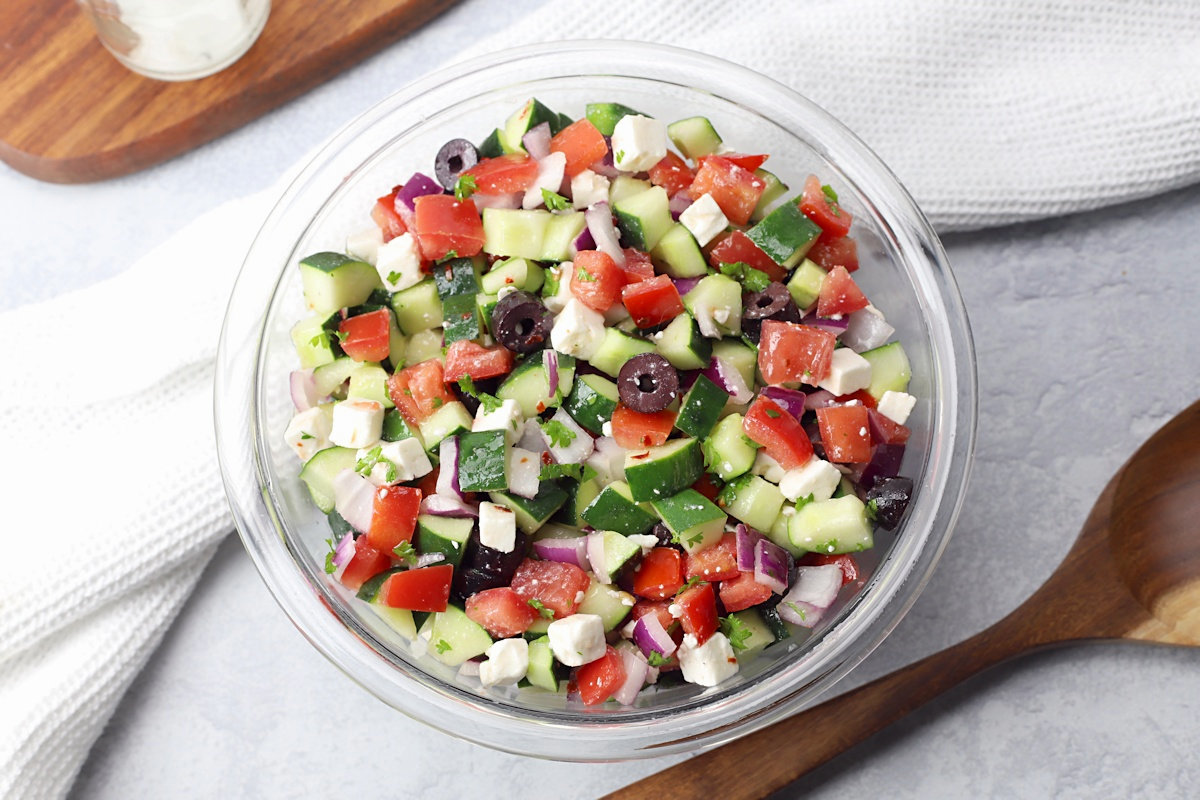 Overhead view of a glass bowl filled with fresh vegetable salad with a serving spoon.