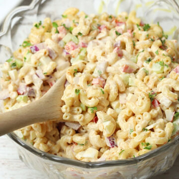 Glass bowl of macaroni salad with a wooden spoon.