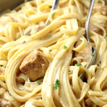 Serving spoon and fork picking up alfredo pasta and chicken.
