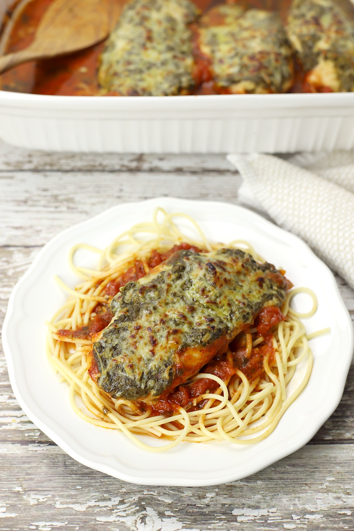 A plate of spaghetti topped by chicken and tomato sauce.